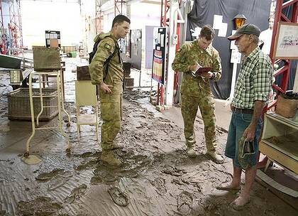 Costly … Corporal Aaron Hayes and Lieutenant Grant Young with volunteer Brian McCarroll in the flooded town of Mitchell.