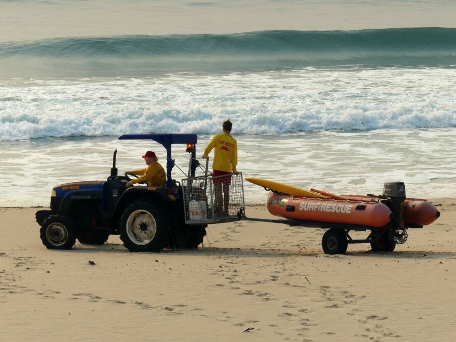 Urunga SLSC long term member Craig Delahunty driving the tractor with the gear onto the beach for setup, with young patroller Drew Clark in the back